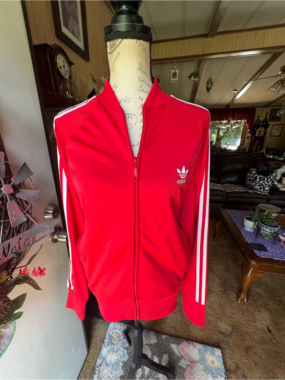 Women’s red Adidas track jacket features white three-stripe down the sleeves.